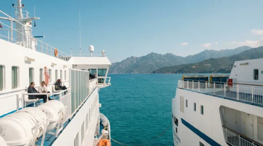 Ferry naviguant vers la Corse en Méditerranée avec côte montagneuse en arrière-plan